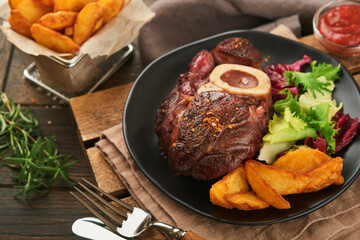 Steaks Osso Buco. Sliced beef grilled Osso Buco or porterhouse meat steak with garnished with salad and french fries on black marble board on old wooden background.