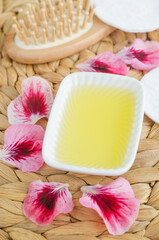 Small white bowl with cosmetic (massage, cleansing) aroma oil and geranium flower petals. Natural skin care, homemade spa and beauty treatment recipe.