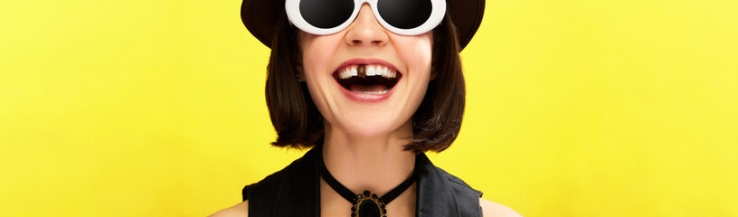 Cropped image of woman in sunglasses smiling with one chocolate tooth against yellow background. Concept of pop art, creativity, food, inspiration, dental care. Banner. Copy space for ad