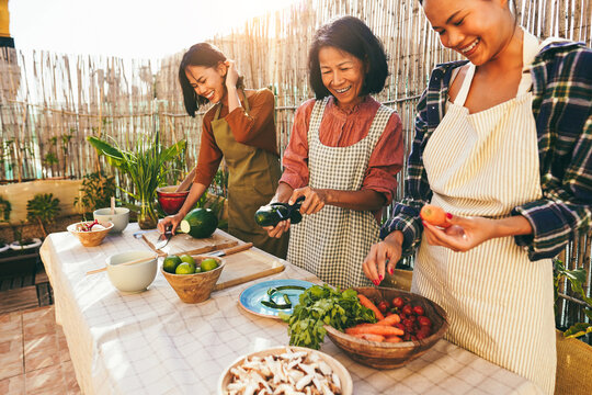 Asian family cooking together at home patio outdoor - Mother and two daughters having fun preparing dinner at house backyard - Main focus on center woman face