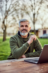 Fototapeta premium Portrait of a smiling senior businessman working over the laptop in nature.