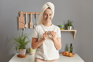 Morning coffee. Cosmetic procedures. Attractive happy young woman posing in kitchen with towel on...