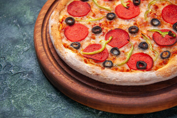 Delicious pizza on wooden cutting board on the left side on isolated dark background with free space in close up shot