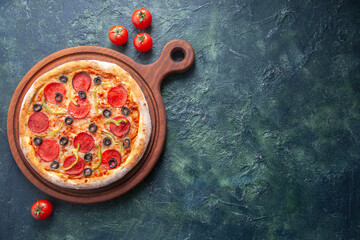 Homemade pizza on wooden cutting board and tomatoes on isolated dark background