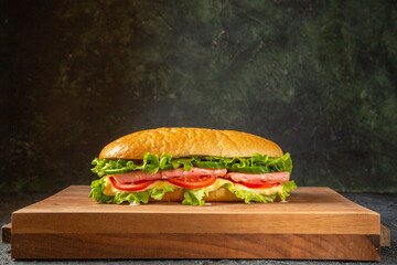 Homemade sandwiches on wooden cutting board on black distressed background