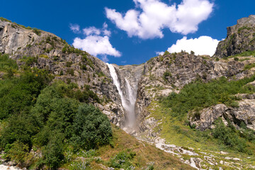 Majestic beautiful bright summer view of the mountain peaks and the Shdugra waterfall, Mazeri in the mountains of Upper Svaneti, Georgia. Conceptual background of the beauty of nature.