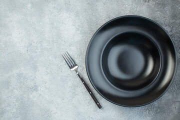 Black dinnerware set and fork on the left side on isolated gray ice background with free space