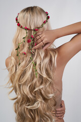 Naklejka premium Close-up shot of a young blonde woman with a handmade wreath decorated with pink flowers and twigs. A beautiful girl with long hair with a wreath on her head is on a light background. Back view.