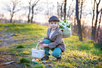 Beautiful stylish toddler child, boy, playing with Easter decoration in the park, springtime