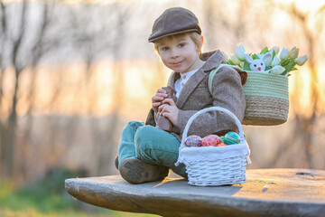 Beautiful stylish toddler child, boy, playing with Easter decoration in the park, springtime