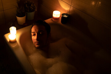 Handsome man bathing in the candlelight. Self care and spa concept	