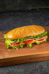 Close up view of delicious homemade sandwich on wooden cutting board on black distressed background