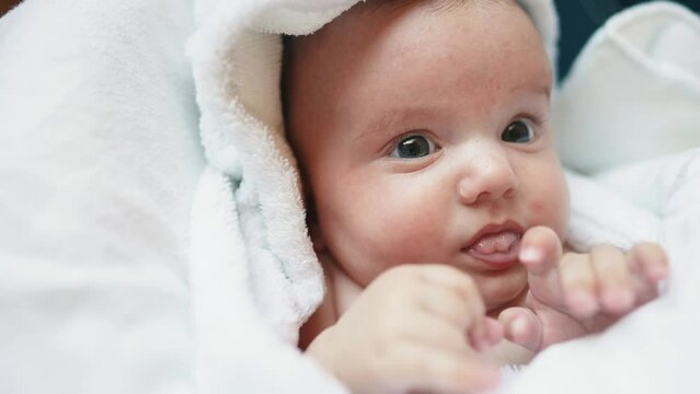 infant girl a newborn sucking thumb. happy family kid dream concept. close up cute newborn baby wrapped in bath lifestyle towel at home indoors. daughter a small child sucks his thumb after bathing