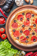 Delicious homemade pizza on wooden cutting board tomatoes garlic ketchup green bundle on dark background