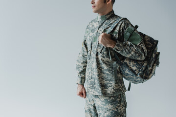 Fototapeta premium cropped view of serviceman in army uniform standing with backpack isolated on grey.