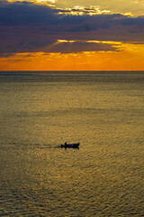 kleines Boot auf offenem Meer in der roten Abendsonne hinter Wolken
