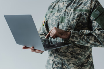 cropped view of soldier in army uniform using laptop isolated on grey.