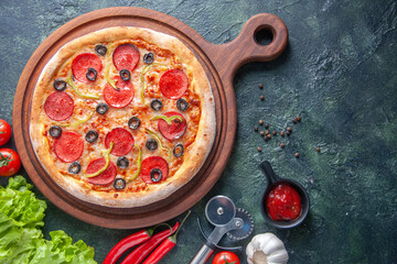 Fototapeta na wymiar Delicious homemade pizza on wooden cutting board tomatoes ketchup green bundle on dark background
