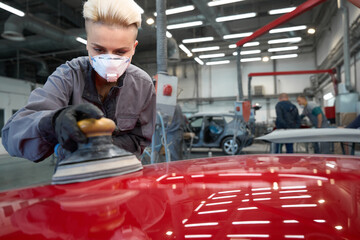 Woman polishing car with power buffer machine in service center