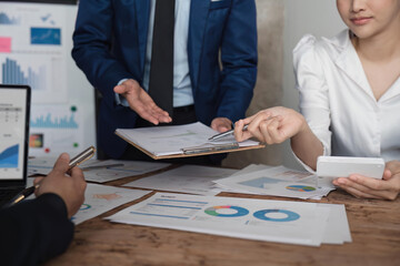 Business team using a calculator to calculate the numbers of statistic business profits growth rate on documents analyzing graph data, desk in the office