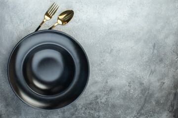 Elegant cutlery set under black dinnerware set on the right side on isolated gray ice background with free space