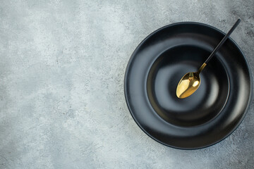 Elegant spoon on black dinnerware set on the left side on isolated gray ice background with free space