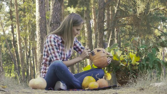 pretty woman paints a pumpkin in a pine forest. Halloween preparations