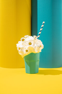 Creamy milkshake with daisy flowers and paper straw on yellow and blue background.