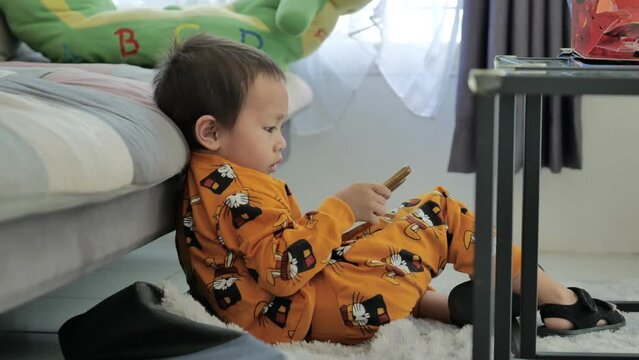 Little boy playing and watching smartphone while sitting on living room shofa
