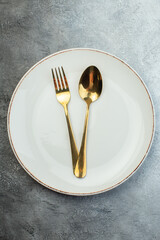 Golden cutlery set on white plate on gray background with distressed coarse-grained gradient surface