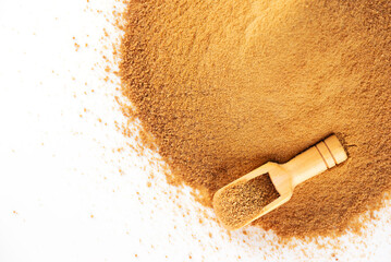 Heap with a wooden scoop with unrefined cane sugar Panela on a white background.