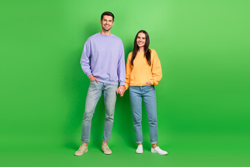 Full length photo of sweet adorable married couple wear sweatshirts walking holding arms palms isolated green color background