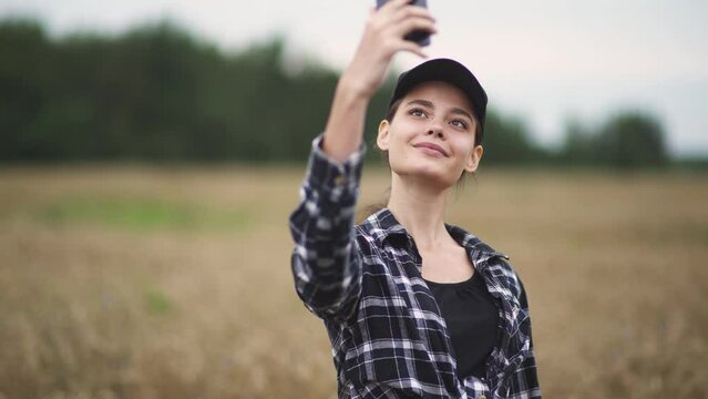 Countryside, pretty woman farmer standing in a field of rye and takes selfie pictures on a smartphone, blurred background.