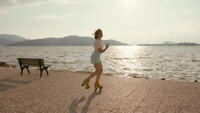 Slim athletic woman roller-skate on retro quads roller skates near sea. Cheerful carefree young woman rollerblading along coastline