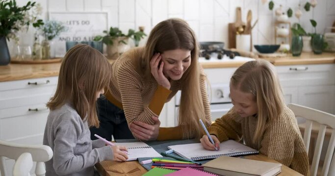 Smiling young mother standing at table and helping children in solving mathematics problems at home