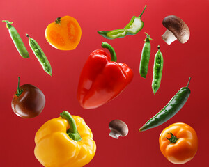 Colorful vegetables arranged in the air on a bright red background.