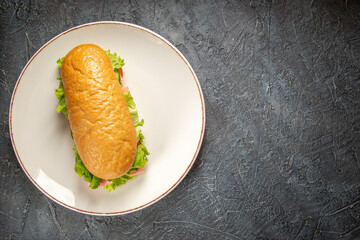 Top view of delicious homemade sandwich on a white plate on the right side on black distressed background with free space