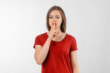 Brunette girl showing of silence gesture, holding finger to lips asking keep secret from boyfriend. Silence and secret concept. Winsome female model in red t shirt posing over white studio background