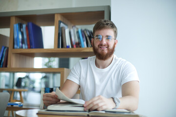 Happy young man read book in library, college or university student prepare to exam in glasses and smile