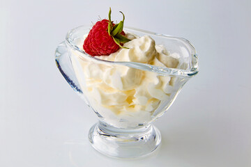 Red raspberries in a glass gravy boat with cream on a white background