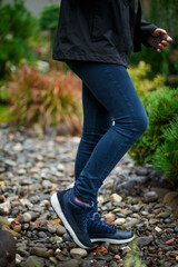 Blue leather sneakers with a white sole and blue laces, shod on the girl's feet, stand on pebbles...