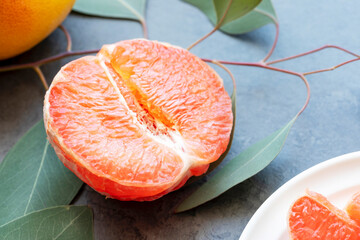 Half of a fresh, juicy grapefruit, sliced grapefruit on a plate and a whole grapefruit on a dark marble background with leaves. Citrus fruits is immune boosting food. Healthy food