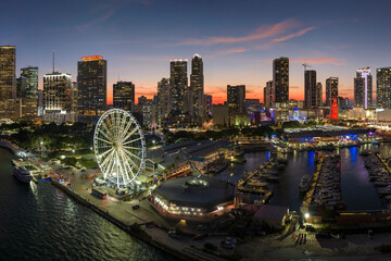 Miami marina harbor and skyscrapers of Brickell, city financial center. Skyviews Miami Observation Wheel at Bayside Marketplace with reflections in Biscayne Bay water and US urban landscape at night - obrazy, fototapety, plakaty