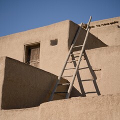 Ladders propped up against an adobe-style house, with a blue sky in the background