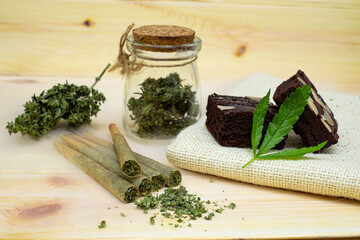 Pre-Roll marijuana joints and cake brownies with cannabis buds in a clear glass jar laying on the...