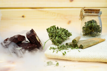 Pre-Roll cannabis joints and cake brownies with cannabis buds in a clear glass jar laying on the sackcloth