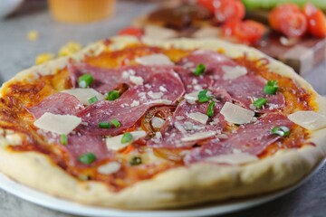 Freshly made pizza with tomatoes, melted cheese and meat displayed on a wooden table