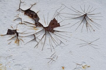 Close-up view of a white wall with chipped paint and rust, revealing a metal surface beneath