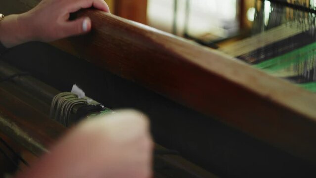 Woman prepares early stages of hand weaving on loom with white cloth