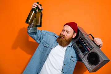 Photo of relaxed young virile man red beard wear beanie hat hold beer bottles listen dj boombox nostalgia party isolated on orange color background